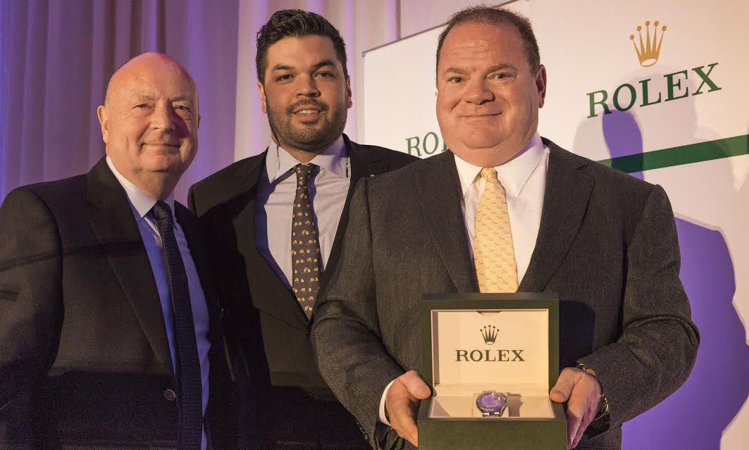 Chip Ganassi holds the Rolex watch signifying the winner of the 2015 Rolex Bob Snodgrass Award of Excellence presented by Harrison Snodgrass (left) and Rolex Watch USA President and CEO Stewart Wicht. [Rolex/Tom O'Neal image]